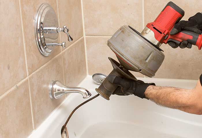 Plumber using a drain snake to unclog a bathtub